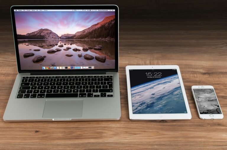 Laptop, tablet, and smartphone arranged on a wooden desk.