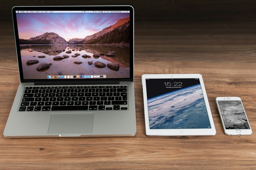 Laptop, tablet, and smartphone arranged on a wooden desk.