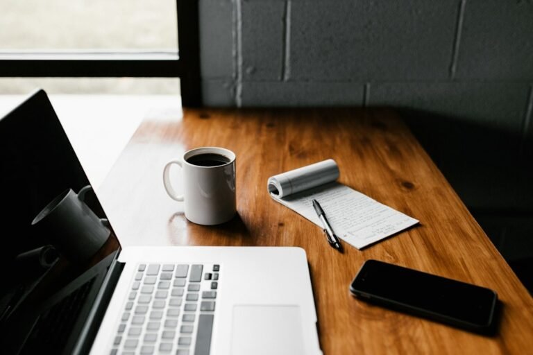 Laptop and smartphone beside a notebook on a wooden table.